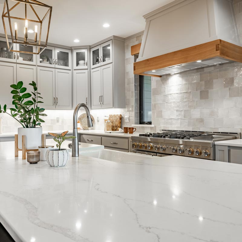 Large kithchen with white countertops, grey cabinets, stainless appliances, large white porcelain double sink farmhouse style.